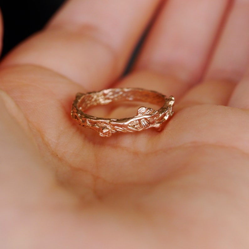 Pu&ograve; includere: Un delicato anello d'oro con un designo a ramo e foglia. L'anello &egrave; realizzato in metallo liscio e lucido e ha un aspetto naturale e organico.