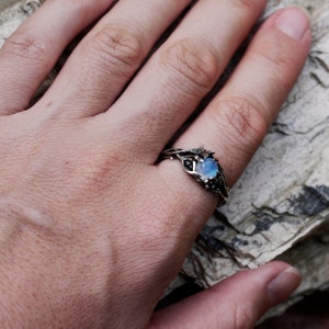 May include: A silver ring with a moonstone set in a twisted vine design. The ring is on a hand, with the background out of focus.