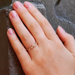 Pu&ograve; includere: Un anello d'oro con un delicato design a foglia. L'anello &egrave; indossato sul dito di una mano con smalto rosa.