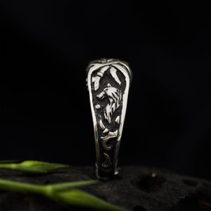 May include: A silver ring with a detailed design of a wolf's head and other intricate patterns. The ring is shown on a dark background.
