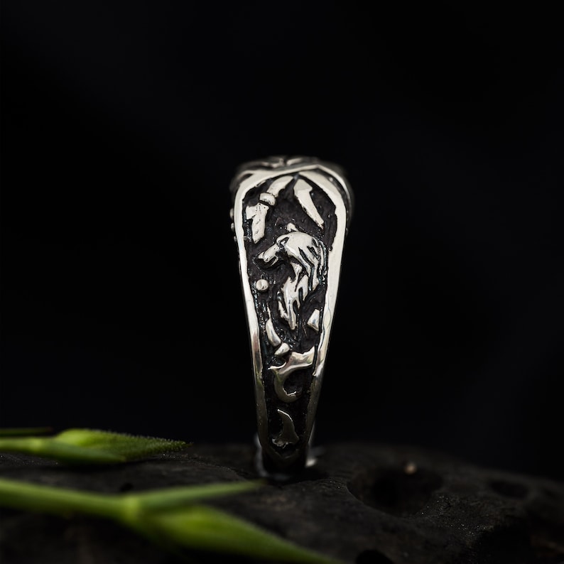 May include: A silver ring with a detailed design of a wolf's head and other intricate patterns. The ring is shown on a dark background.