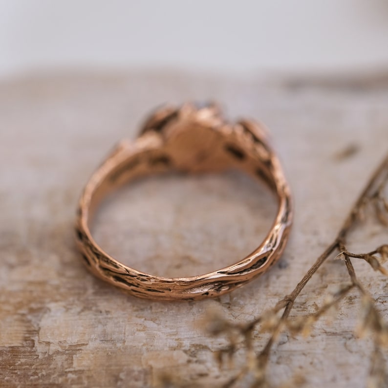 Puede incluir: Un anillo de oro rosa con una banda texturizada que se asemeja a la corteza de un &aacute;rbol. El anillo est&aacute; engastado con una sola piedra.