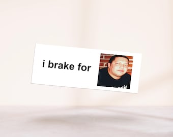 May include: A white rectangular sign with the text "i brake for" and a photo of a man in a black shirt. The man is in front of a brick wall. The sign is slightly angled.