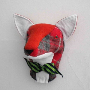 May include: A red, grey and white plaid fox head with a green and black bow tie. The fox head is made of fabric and is a wall decoration.
