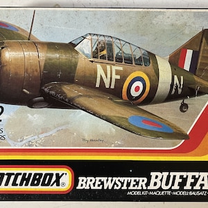 May include: A Matchbox 1/72 scale model kit of a Brewster Buffalo fighter plane. The model is painted in camouflage colors with the markings "NF" and a roundel. The box art features a detailed illustration of the plane in flight.