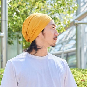 This is a Japanese male wearing a casualbox cotton slouch beanie for summer, Mustard Yellow slouchy beanie for summer. A slouchy beanie for womens and men. A slouchy beanie that is available in rose pink, black, and white. A slouchy beanie for adults