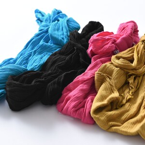 May include: Four fabric scarves in different colors: blue, black, pink, and yellow. The scarves are made of a soft, textured material and are arranged in a pile.