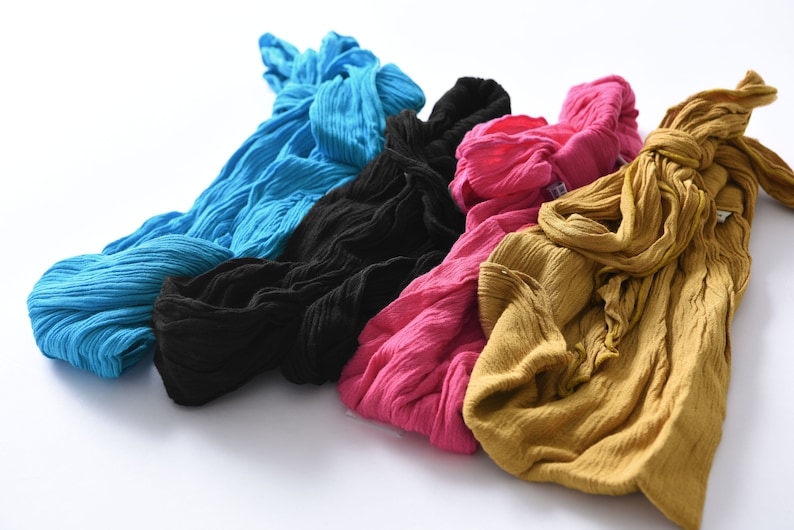 May include: Four fabric scarves in different colors: blue, black, pink, and yellow. The scarves are made of a soft, textured material and are arranged in a pile.