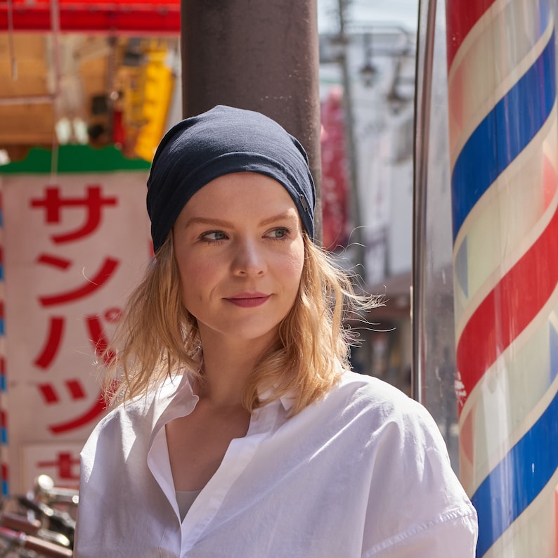 Pode incluir: Uma mulher com cabelo loiro est&aacute; usando uma boina azul marinho e uma camisa branca de bot&otilde;es. Ela est&aacute; em p&eacute; na frente de um poste listrado vermelho, branco e azul.