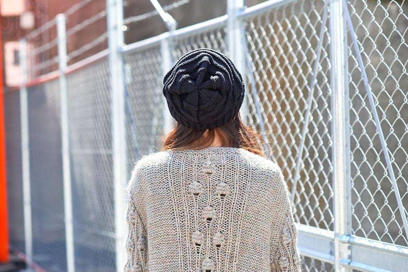May include: A person wearing a black knit beanie and a beige knitted sweater with a cable knit pattern.