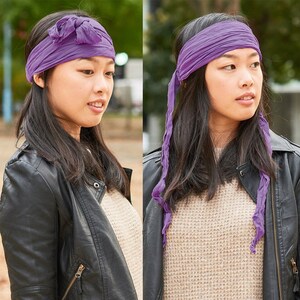 May include: A purple fabric headband tied in a knot on top of the head. The headband is worn by a person with long dark hair and a black leather jacket.