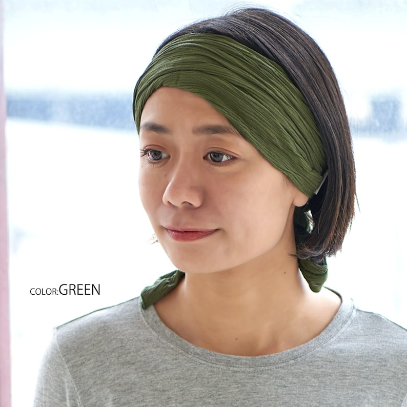 May include: A green fabric headband worn by a person with short dark hair. The headband is tied in a knot at the back of the head.  COLOR: GREEN