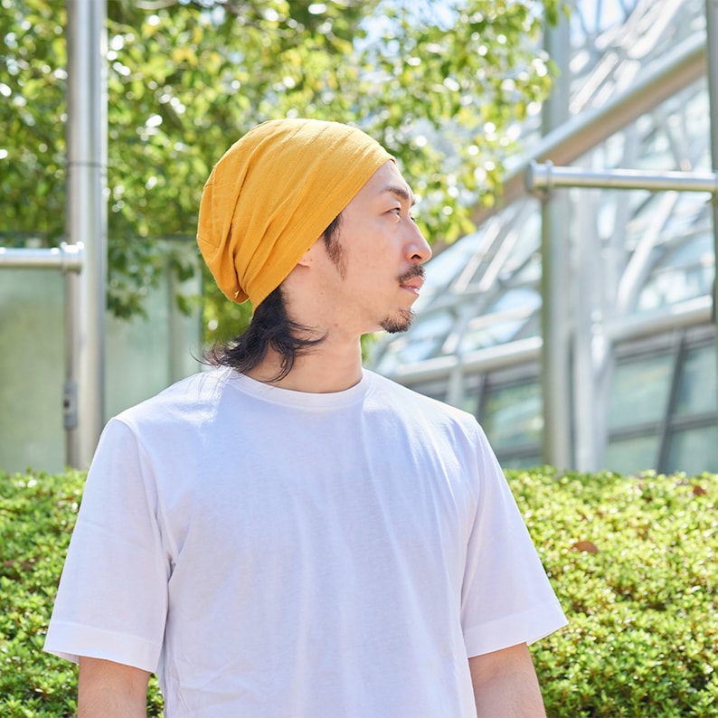 This is a Japanese male wearing a casualbox cotton slouch beanie for summer, Mustard Yellow slouchy beanie for summer. A slouchy beanie for womens and men. A slouchy beanie that is available in rose pink, black, and white. A slouchy beanie for adults