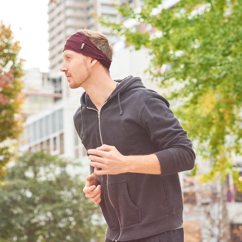 May include: A man wearing a maroon headband and a black hooded sweatshirt is running outdoors.