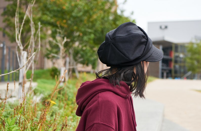 K&ouml;nnte beinhalten: Eine Person tr&auml;gt eine schwarze Newsboy-M&uuml;tze mit einem weinroten Kapuzenpullover.