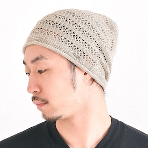 May include: A beige knit beanie with a textured, open-weave pattern and a smooth, solid-knit border at the base. The hat features a small, rectangular metallic tag attached to the side, showcasing a lightweight, breathable construction.