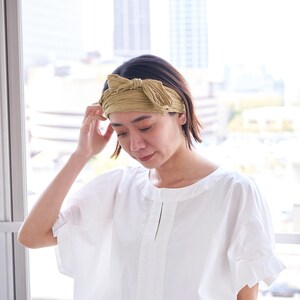May include: A woman wearing a white shirt with a light brown headband tied in a bow on her head.