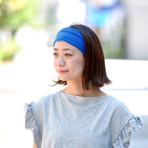 May include: A woman with short brown hair is wearing a gray t-shirt with ruffled sleeves and a blue headband.