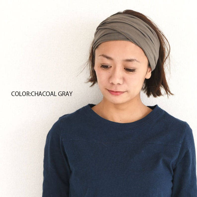 May include: A woman wearing a charcoal gray headband. The headband is made of a soft, stretchy fabric and is tied in a knot at the top of her head. She is wearing a dark blue long-sleeved shirt.