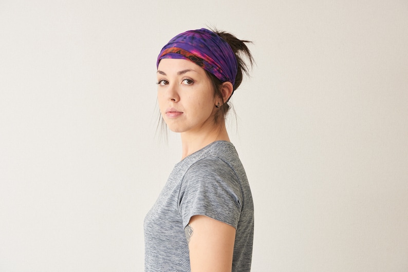 Puede incluir: Una diadema tie-dye morada y naranja es usada por una persona con cabello oscuro. La diadema est&aacute; envuelta alrededor de la cabeza y est&aacute; hecha de un material suave y flexible. La persona lleva una camiseta gris.