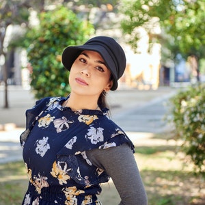 Puede incluir: Una mujer con un sombrero negro, un vestido de estampado floral y una camisa de manga larga gris.