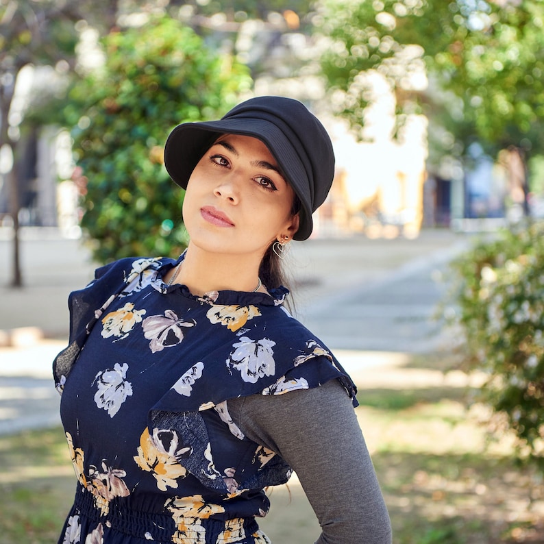 Puede incluir: Una mujer con un sombrero negro, un vestido de estampado floral y una camisa de manga larga gris.