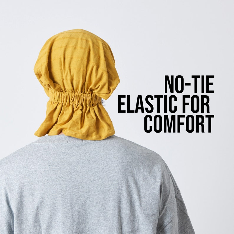 K&ouml;nnte beinhalten: Ein gelber Stoffhut mit einem Gummiband am unteren Rand. Der Hut wird auf dem Kopf einer Person getragen. Der Text "NO-TIE ELASTIC FOR COMFORT" ist auf wei&szlig;em Hintergrund gedruckt.