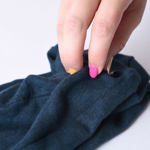 May include: A hand with pink and yellow nail polish is shown holding a folded piece of dark blue fabric.
