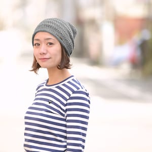 May include: A grey knit beanie with a delicate openwork pattern and a long-sleeve shirt featuring horizontal navy blue and white stripes with a small black heart-shaped logo on the upper left chest area of the garment.