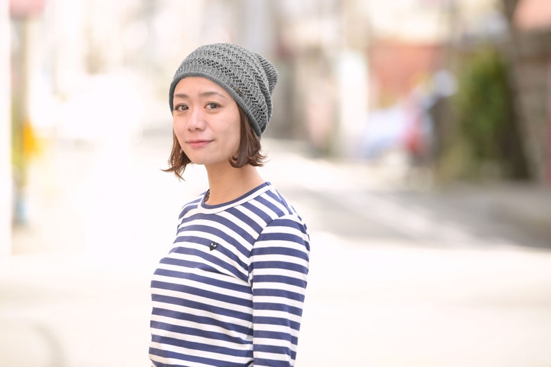 May include: A grey knit beanie with a delicate openwork pattern and a long-sleeve shirt featuring horizontal navy blue and white stripes with a small black heart-shaped logo on the upper left chest area of the garment.