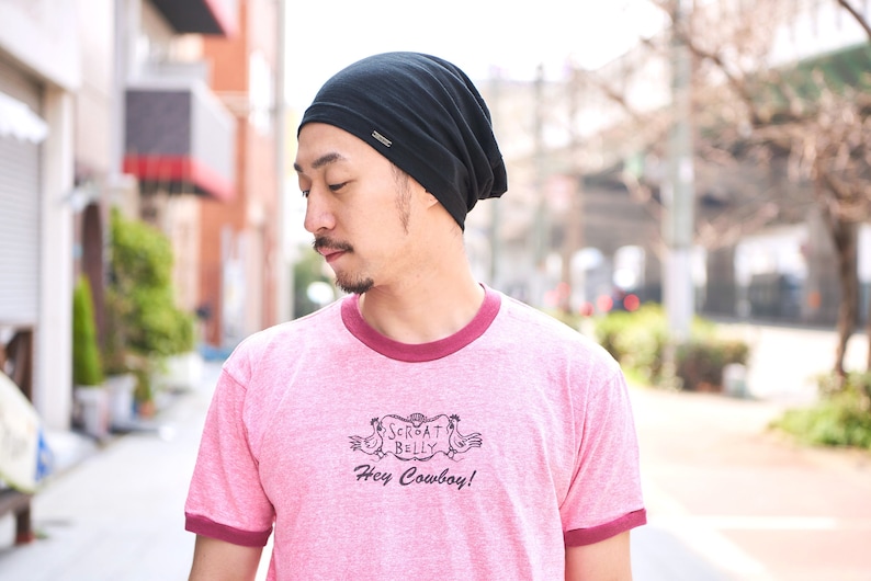 Pode incluir: Uma pessoa usando um gorro preto com uma camiseta rosa que diz "Scrat Belly Hey Cowboy!"