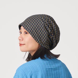May include: A woman wearing a black and yellow striped beanie hat. The hat is made of a soft, stretchy fabric and has a slouchy fit.