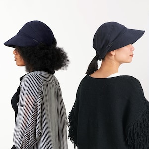 Puede incluir: Dos mujeres con sombreros de sol azul marino de ala ancha. La mujer de la izquierda lleva una camisa a rayas y la mujer de la derecha lleva un su&eacute;ter negro con flecos.
