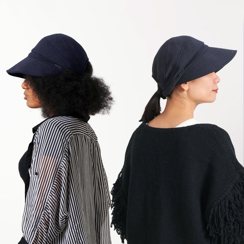 Puede incluir: Dos mujeres con sombreros de sol azul marino de ala ancha. La mujer de la izquierda lleva una camisa a rayas y la mujer de la derecha lleva un su&eacute;ter negro con flecos.