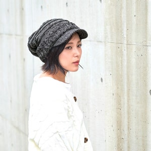 May include: A woman wearing a gray knitted beanie with a brim and a white sweater.