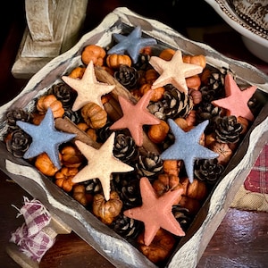 Op de afbeelding: Een houten doos gevuld met herfstdecoraties, waaronder mini-pompoenen, dennenappels en kaneelstokjes. De doos bevat ook negen stervormige potpourri-stukken in tinten blauw, rood en beige.