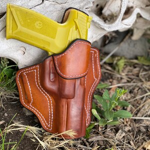 May include: A brown leather holster with white stitching, designed to hold a yellow handgun with the word "RUGER" printed on the side.
