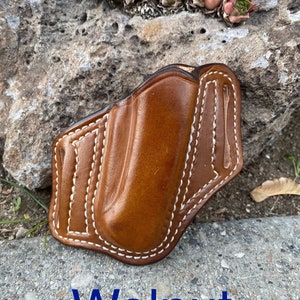 May include: A brown leather holster with white stitching. The holster is designed to hold a small pocket knife or other small tool. The text "Walnut" is printed below the holster.