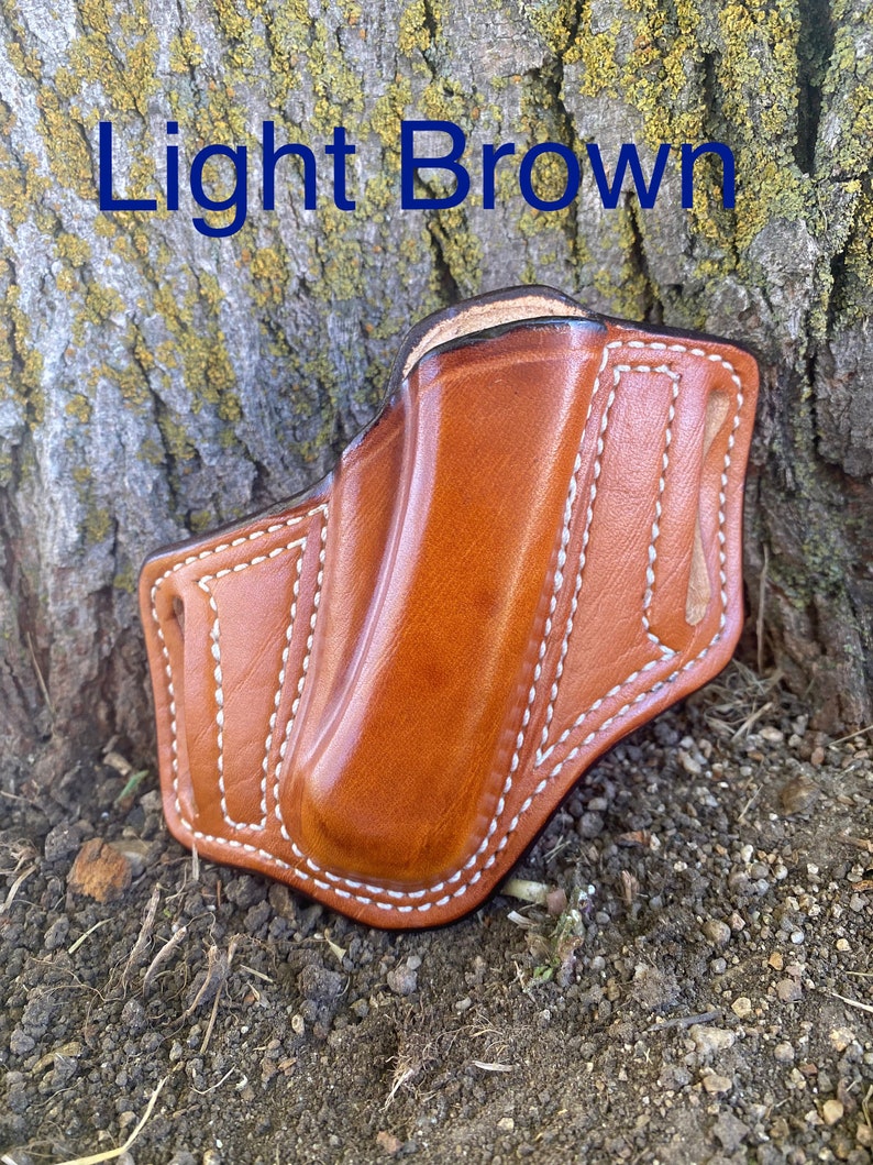 May include: Light brown leather holster with white stitching. The holster is designed to hold a small pocket knife or other similar tool.