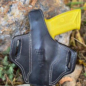 May include: Black leather holster with white stitching and the text "Ruger EC9S" and an American flag. A yellow Ruger EC9S pistol is partially visible in the holster.