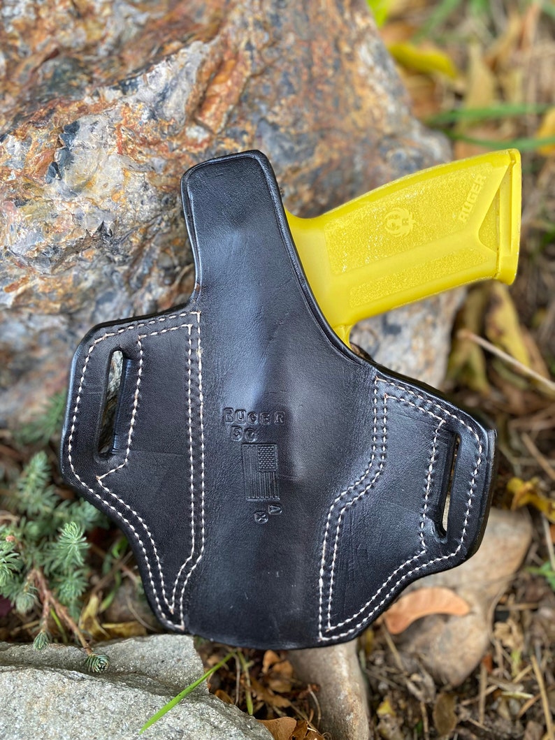 May include: Black leather holster with white stitching and the text "Ruger EC9S" and an American flag. A yellow Ruger EC9S pistol is partially visible in the holster.