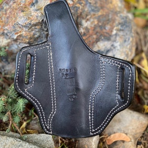May include: Black leather holster with white stitching and the text "Ruger 57" and an American flag design.