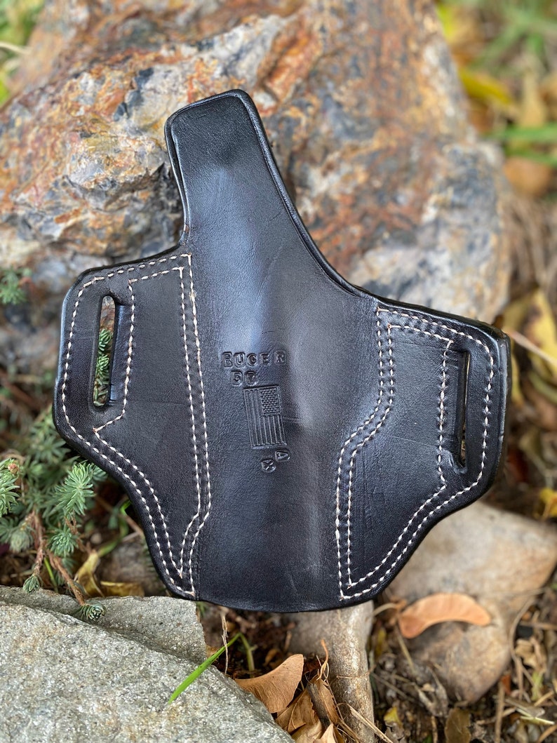 May include: Black leather holster with white stitching and the text "Ruger 57" and an American flag design.