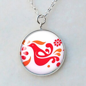 May include: A silver necklace with a round pendant featuring a red bird design with orange accents on a white background. The pendant is approximately 1 inch in diameter and hangs from a delicate silver chain.