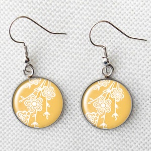May include: A pair of round earrings with a floral design. The earrings have a yellow background with a white floral pattern. The earrings have silver-colored hooks.