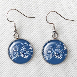 May include: A pair of round dangle earrings with a floral design. The earrings feature a dark blue background with white flowers and foliage. The earring hooks are silver-colored.