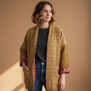 May include: A mustard yellow jacket with a woven pattern, featuring contrasting patterned cuffs in red and white. The jacket has a relaxed fit and is worn over a dark gray shirt and blue jeans. The jacket has pockets.
