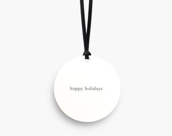 May include: A white round gift tag with black string. The tag has the text "happy holidays" printed on it.
