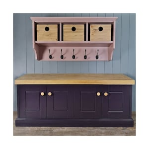 May include: A dark purple cabinet with four doors and wooden knobs. The cabinet has a light wood top and sits on a wooden floor. Above the cabinet is a pink wall-mounted shelf with three wooden boxes and hooks.