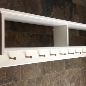 Coat rack with pegs to hang coats. Display / storage shelf divided into two compartments. Painted white.